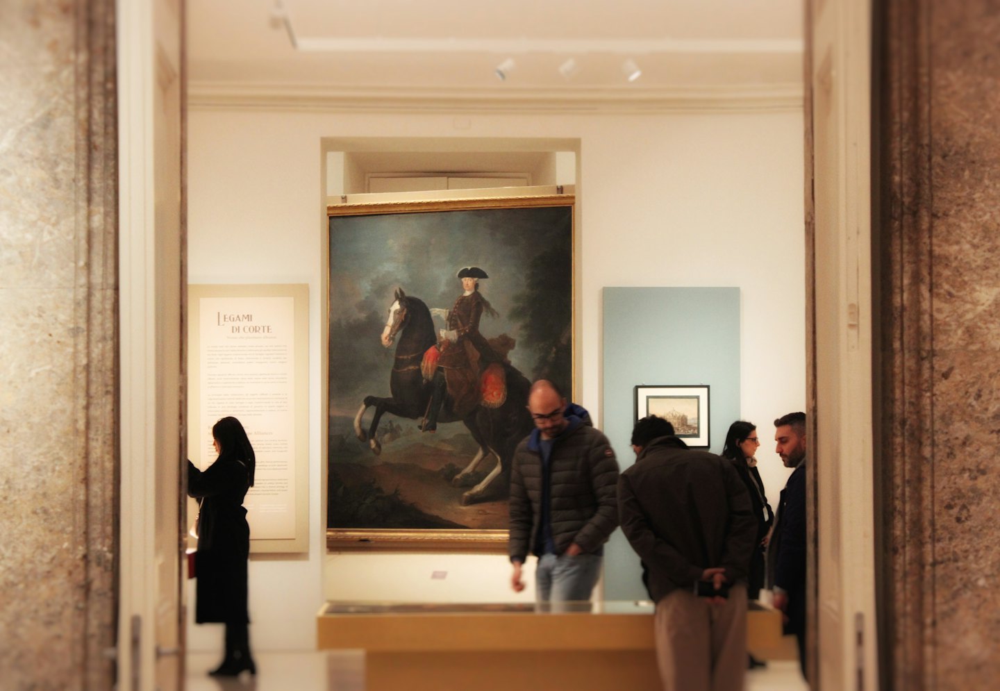 Visitatori che ammirano un grande dipinto a olio incorniciato di un cavallo e un cavaliere.