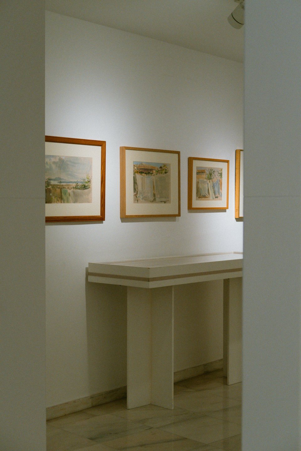 Tre opere d'arte paesaggistica in un corridoio di galleria bianco.